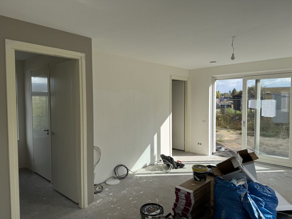 Nieuwe woonkamer tijdens de afwerking, met emmers muurverf, kabels en dozen op de betonvloer