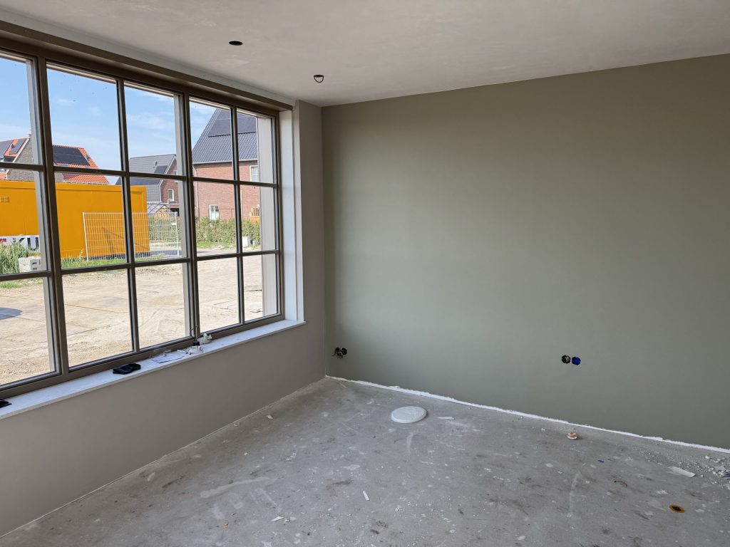 Kamer in een nieuw huis met een egale wand in grijsgroen en een groot raam met roeden