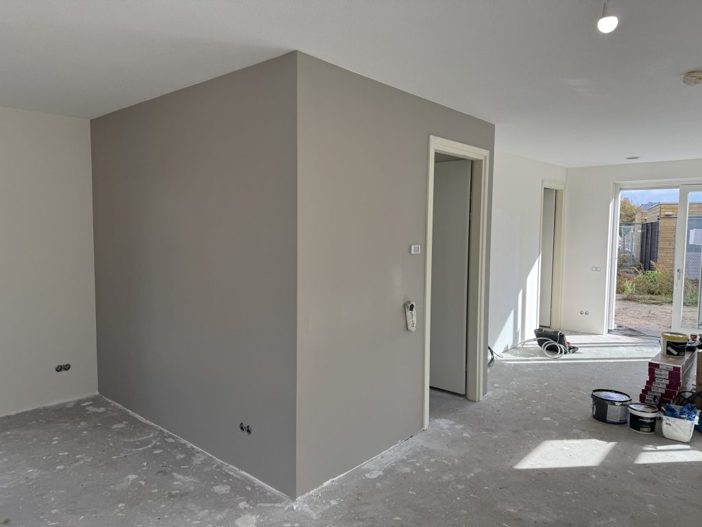 Pas gesausde grijze wand rond een deur in een nieuwbouwwoning, met verfemmers op de vloer