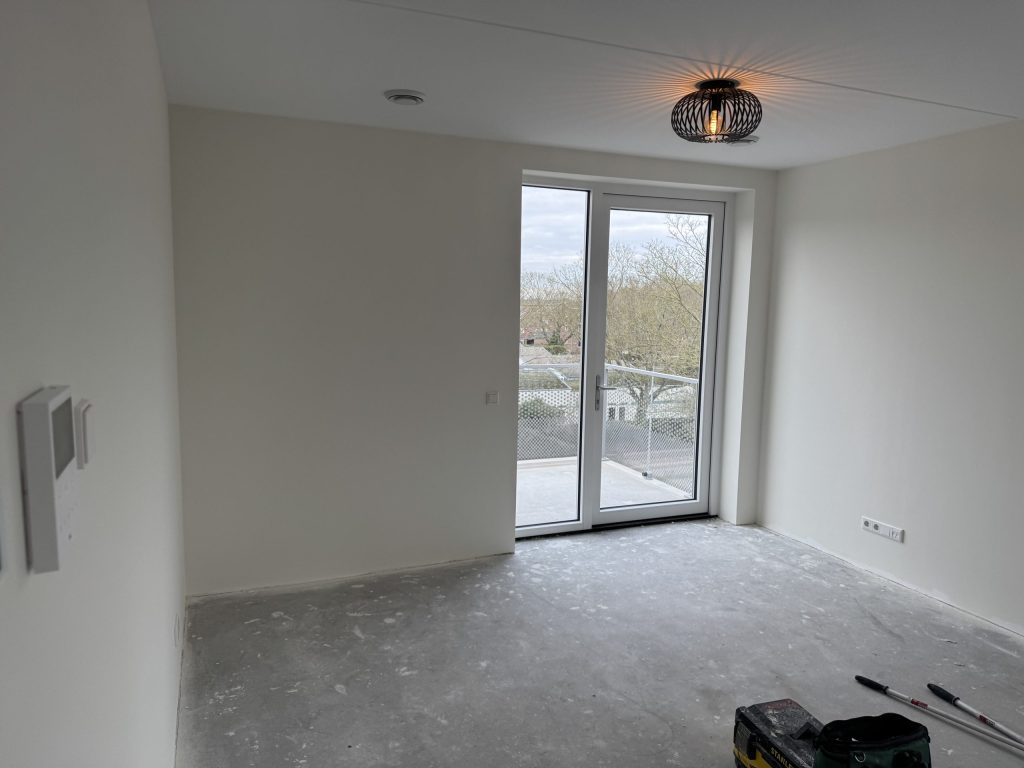 Lege kamer in een nieuw appartement met een balkondeur, betonvloer en uitzicht op bomen