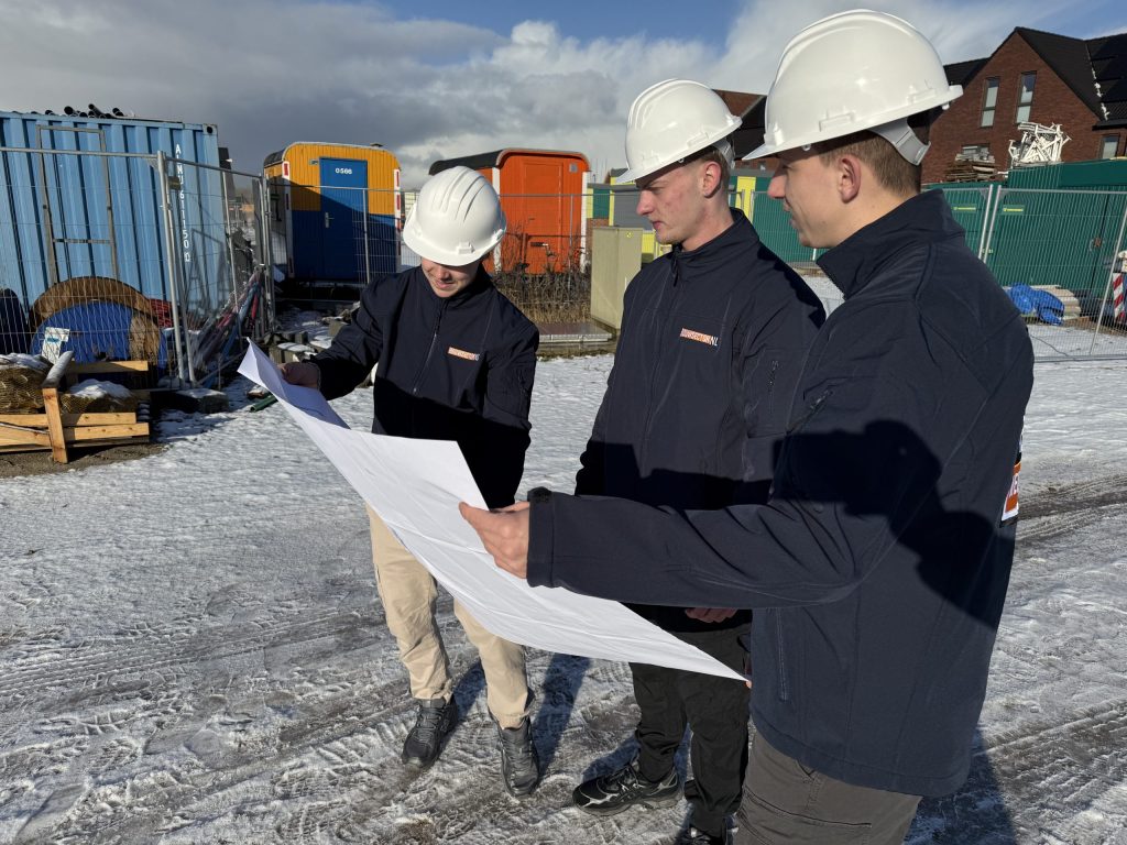 Drie medewerkers van Bouwsector Nederland met witte helmen bekijken een bouwtekening op een besneeuwde bouwplaats